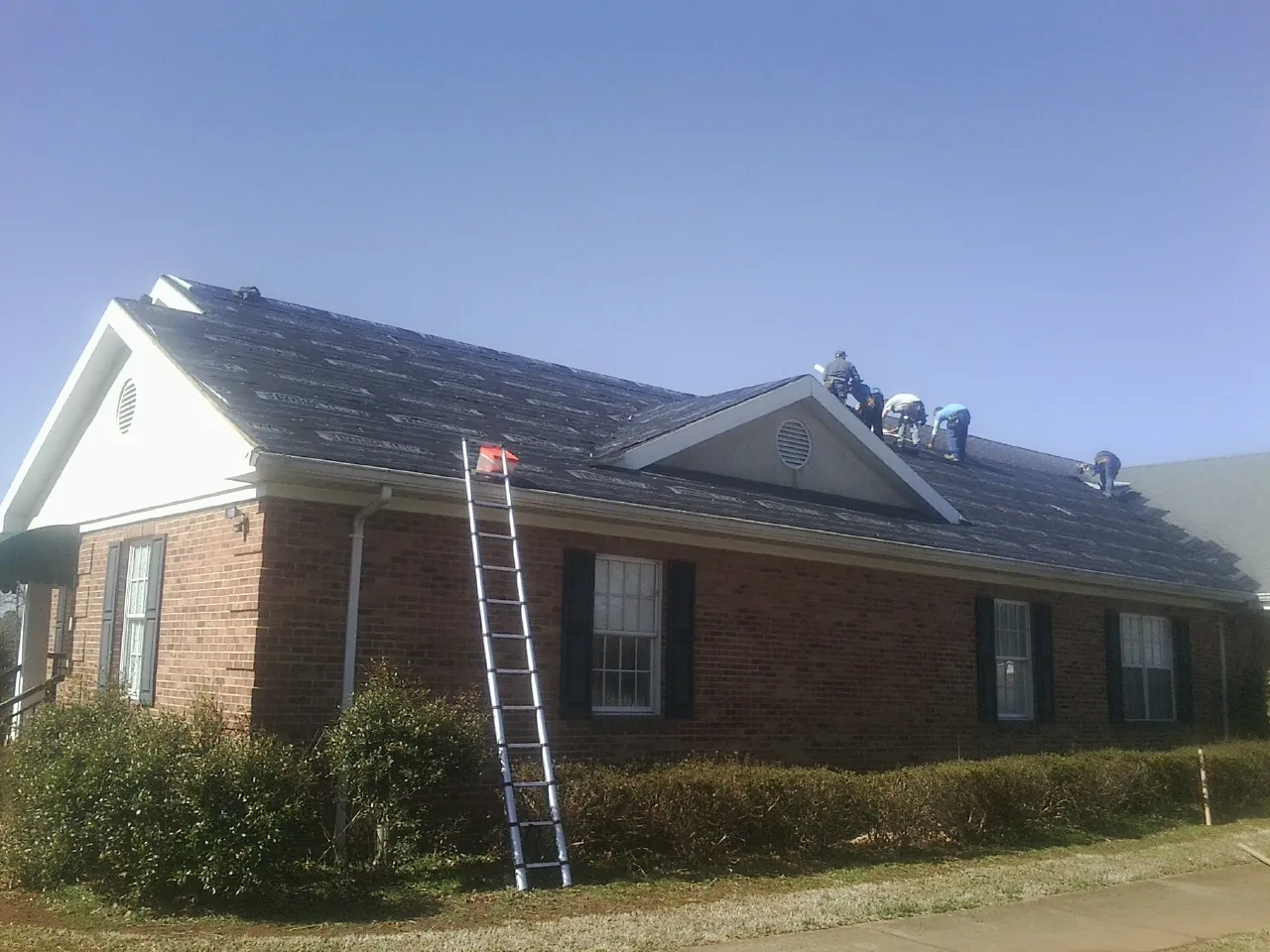 Crew tearing shingles off a brick ranch roof with a ladder set — Emergency Roof Repair work by our crew in Old Town