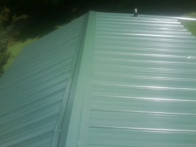New green metal panels meeting at the ridge of a roof — Flat Roof Repair work by our crew in Old Town