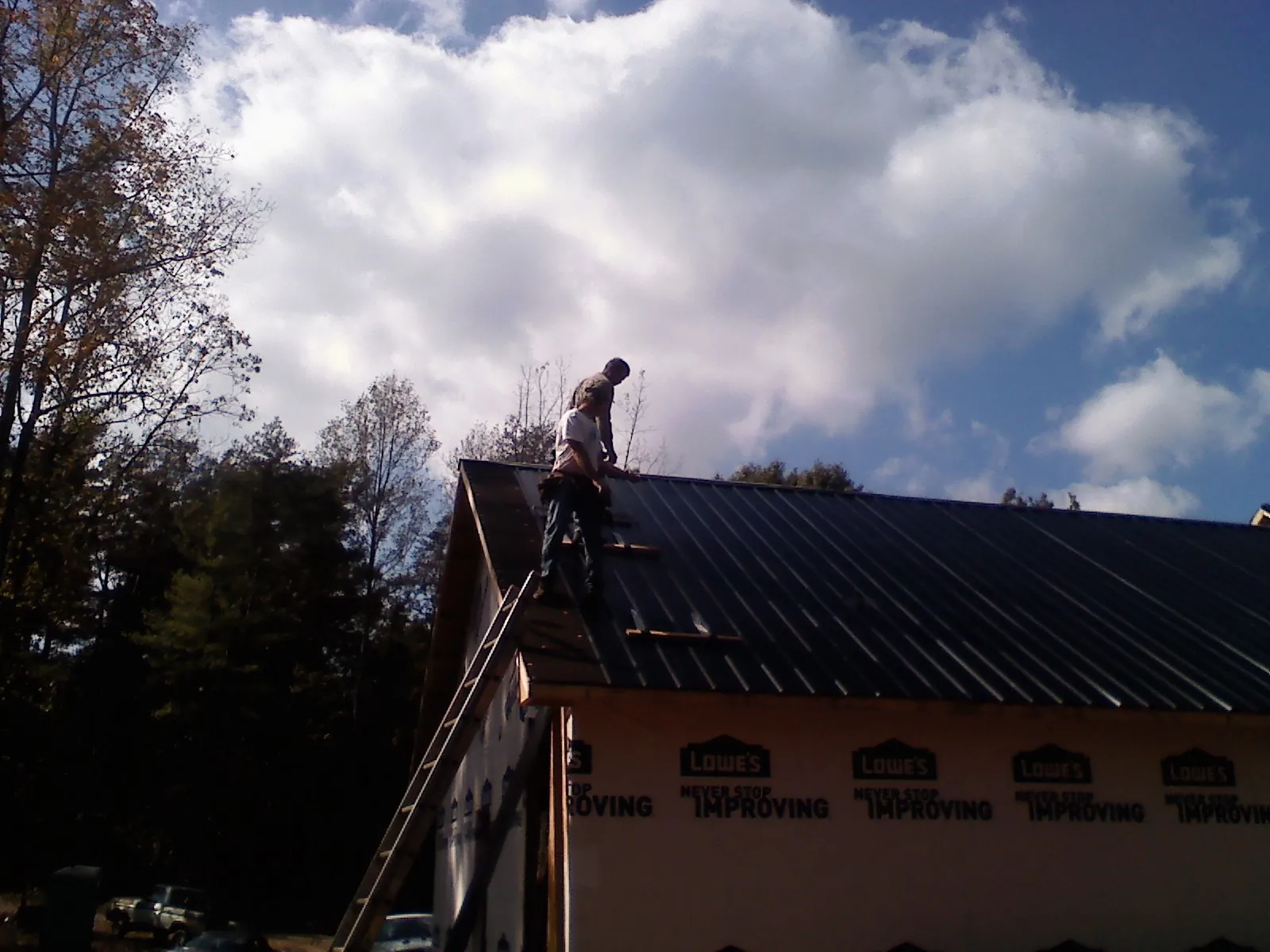 Roofer fastening dark metal panels high against a cloudy sky, from a Roof Inspection job in Old Town