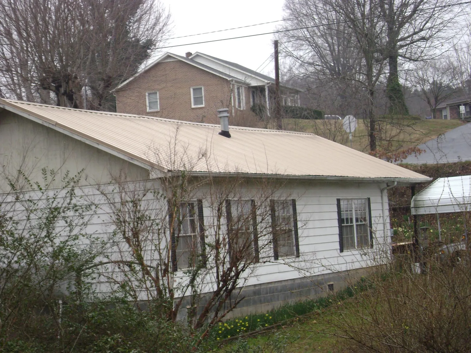 Tan metal roof on a white sided house set into a hillside — Commercial Roofing by Roofing Brothers in Old Town